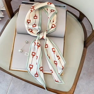 Dettaglio di un foulard in seta bianco con bordi verdi e motivo a morsetto arancione