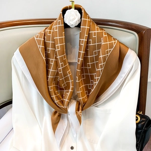 Détail d'un foulard en soie noué en cravate, motif géométrique en caramel et blanc
