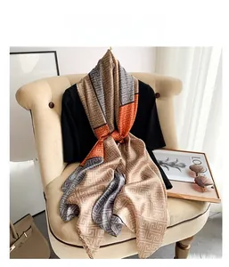 Detail of silk-feel scarf with Greek Key geometric pattern and vibrant orange accents