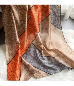 Detail of silk-like scarf featuring orange and khaki geometric Greek key patterns