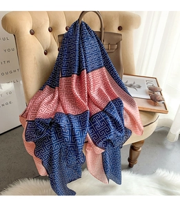 Detail of a navy and pink geometric pattern silk scarf draped on a beige armchair