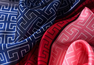 Detail of silk scarf showing deep blue and red Greek key patterns with satin texture