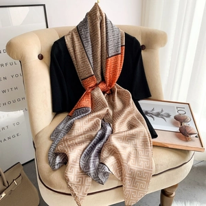 Elegant geometric meander pattern silk shawl in beige and orange on a modern armchair