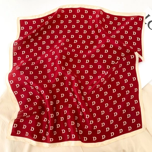 Close-up of red silk square scarf featuring repeat D pattern and cream beige border