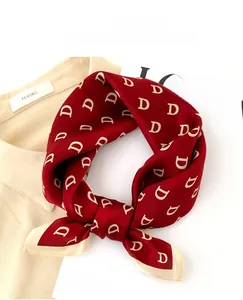 Detail of red silk square scarf with white letter D pattern on beige shirt background