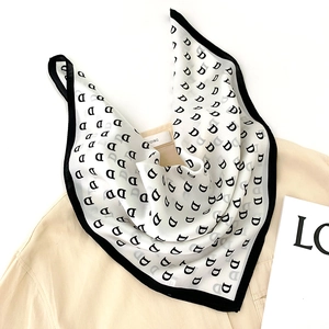 Elegant white silk square scarf with black letter D print on a light beige shirt