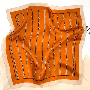 Detail of silk square scarf featuring orange border and golden chain equestrian prints