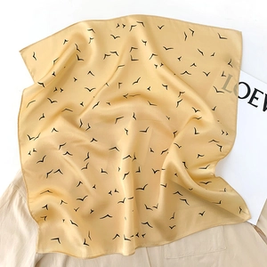 Detailed texture of yellow silk scarf featuring black seagull print on soft fabric