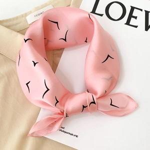 Detail of pink silk scarf with black bird print tied in a bow on a white shirt