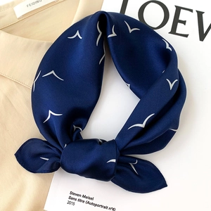 Elegant navy blue silk scarf with seagull print styled on a beige shirt and magazine