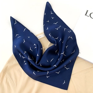 Detail of navy blue silk square scarf with white bird patterns and elegant satin texture