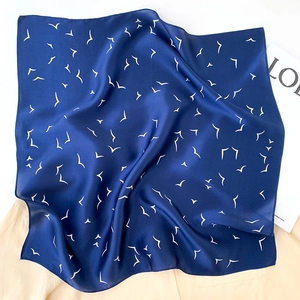 Detail of silk scarf showing navy blue bird pattern and smooth satin texture on fabric