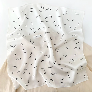 Detail of premium white silk scarf featuring minimalist black seagull print on beige shirt