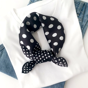 Detailed view of a black silk scarf with white polka dots on a white t-shirt and blue jeans