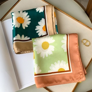 Detail of silk daisy scarves in green and mint shades on a luxury gold-rimmed tray