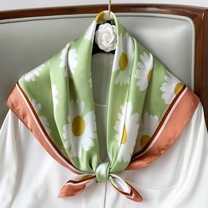 Detail of silk scarf with daisy print, green hue and striped edges on a white shirt