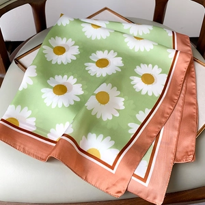 Close-up of silk square scarf featuring white daisies on green with orange pink border