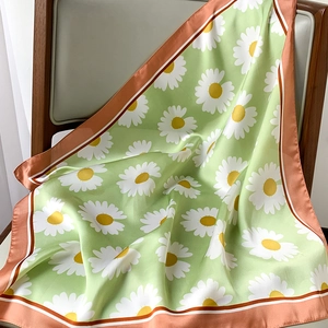 Detail of silk scarf with daisy print draped on wood, showing smooth texture and green luster
