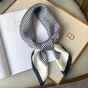 Detail of elegant houndstooth silk scarf tied in a bow on a white magazine and tray