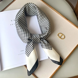 Elegant silk scarf with black and white houndstooth pattern displayed on a gold tray