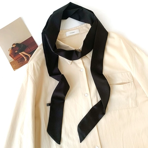 Detail of a sleek black satin skinny scarf paired with a minimalist beige shirt