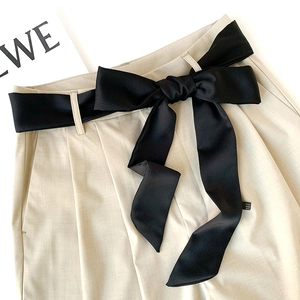Detail of beige high-waist pants featuring a contrast black satin ribbon bow at the waist