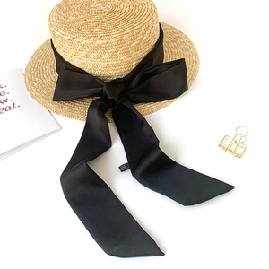 Close-up of flat top straw boater hat with a large black satin bow on white backdrop
