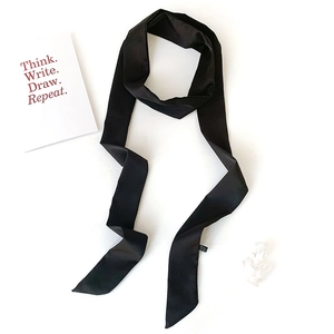 Detail of a sleek black satin skinny scarf and hair ribbon shown on a white minimal setup