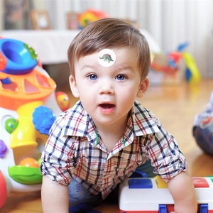 Close-up of a smiling toddler wearing a green dinosaur cartoon sticker on the forehead