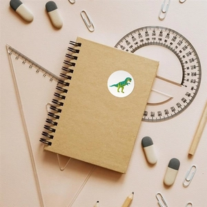 Cartoon green dinosaur sticker applied on a spiral notebook with stationery school supplies