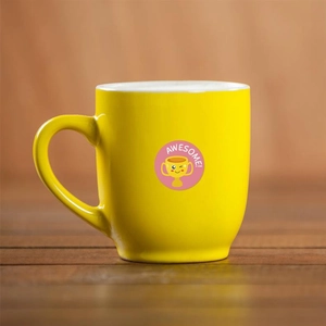 Close-up of yellow ceramic mug with pink Awesome smiley trophy sticker on wooden surface