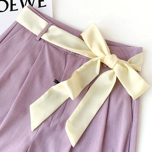 Detail of lavender high-waist trousers with a yellow silk bow tie and pleated waist design
