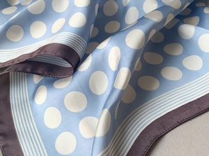 Detail showing the smooth silk-like texture of a light blue polka dot square scarf