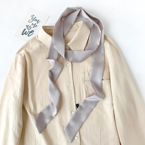Detail of light gray satin skinny scarf styled on a beige shirt with silky texture