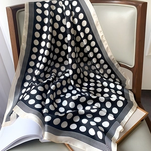 Detailed view of polka dot silk scarf draped on leather chair showing glossy texture