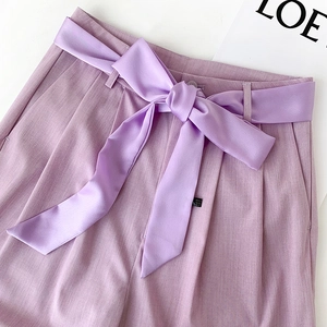 Detail of light purple trousers featuring a decorative satin ribbon tied in a bow at the waist