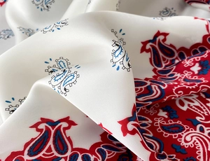 Detailed view of the smooth satin texture and red paisley print on the ivory square scarf