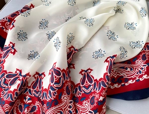Close-up of a paisley print silk scarf in off-white with red and navy contrast borders