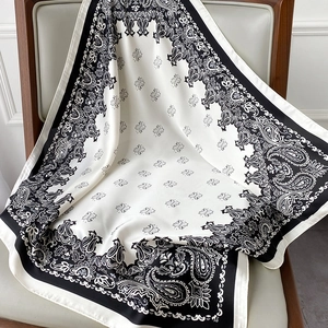 Detailed texture of black and white paisley silk scarf draped on a leather chair