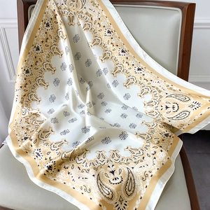 Detail shot of the silky paisley square scarf with golden geometric borders on a chair