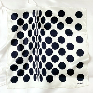 Detail of silk square scarf with black polka dots on cream background showing brand tag