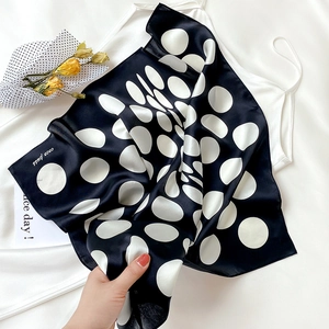 Detailed view of black silk scarf with white polka dots and printed brand logo