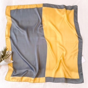 Dettaglio di un foulard di raso bicolore giallo e grigio su sfondo di tessuto bianco