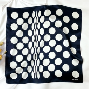 Detailed flat lay of a black and white polka dot silk scarf with elegant brand logo