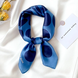 Blue silk scarf with navy polka dots in elegant knot on a white silk background