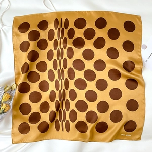 Detail shot of a yellow silk scarf with brown polka dots on a white background