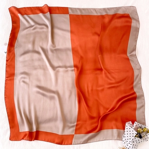 Dettaglio di un grande foulard di raso con design a scacchi color block arancione e crema