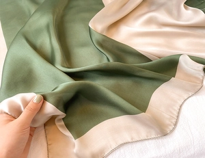 Dettaglio di sciarpa in seta color-block verde erba e champagne con finitura bordi rullati