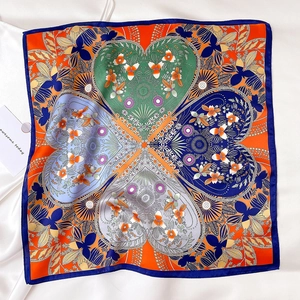 Detail of silk square scarf showing orange clover pattern and blue border on white fabric