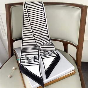 Slim black and white striped silk twilly scarf with geometric patterns on a leather chair